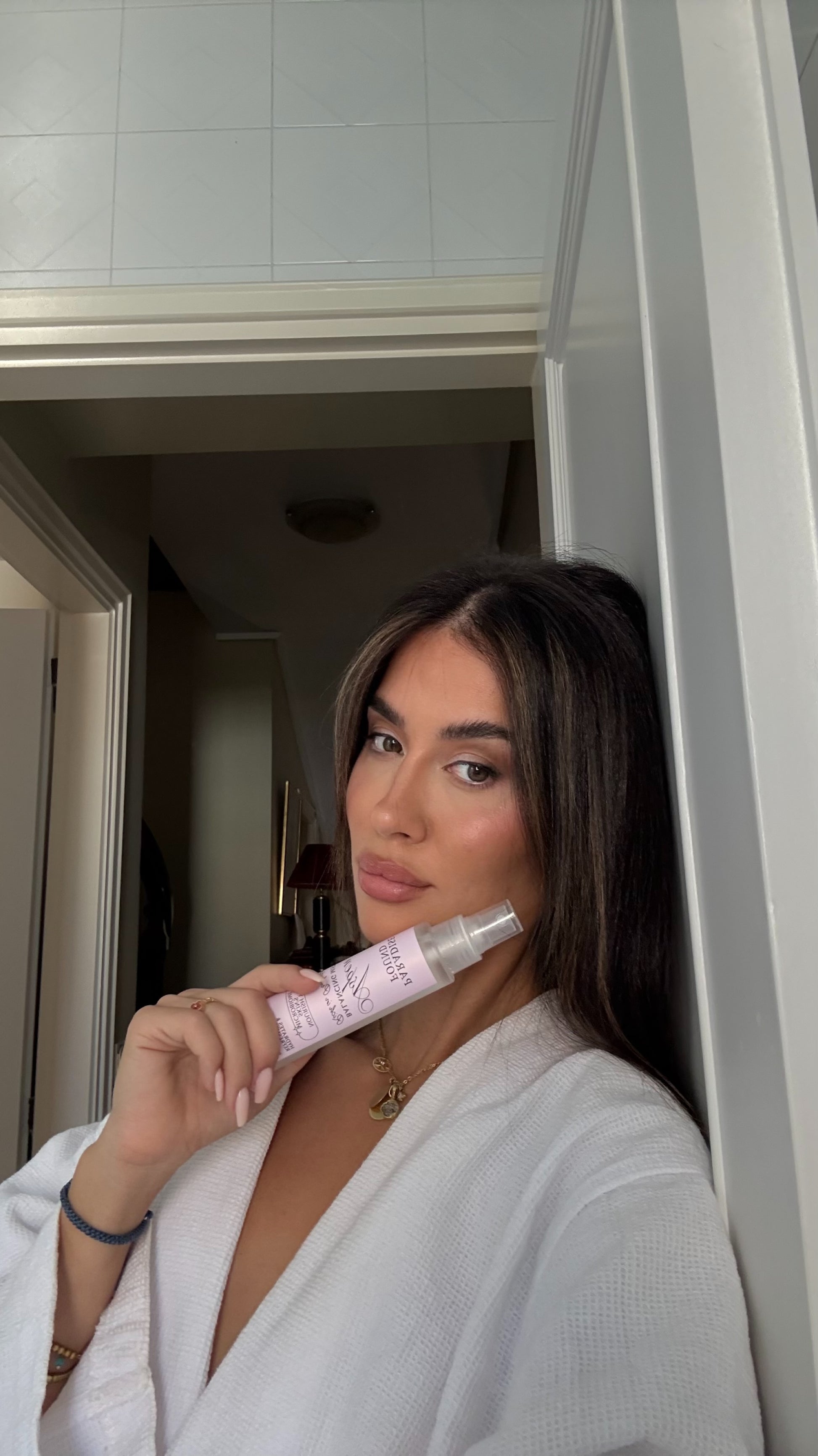 Woman holding a pink skincare product in a bathroom setting